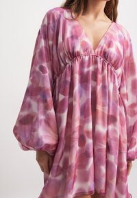 Doorzichtig jurkje met een V-hals, gerimpelde lijf en ballonmouwen. Kenmerkt zich door een roze bloemenpatroon met verschillende tinten en een zachte, vloeiende textuur.