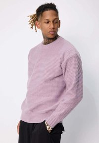 Pull en maille violet clair avec un motif texturé rayé et des poignets côtelés. Il dispose d'un col rond classique et d'une coupe décontractée.