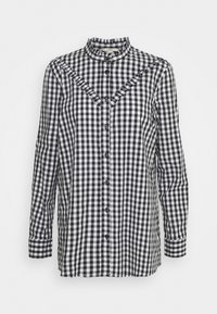 Camicia a maniche lunghe con motivo a quadretti bianco e nero, caratterizzata da un colletto alto e una patta con bottoni neri, vestibilità aderente e dettagli arricciati.