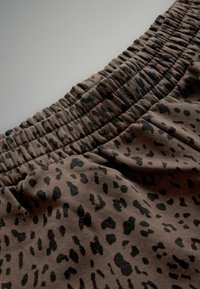 Brunt tyg med svart leopardmönster och en rynkad resår i midjan, vilket skapar en strukturerad och flexibel design.