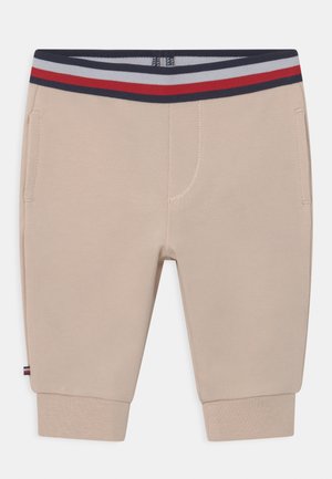 Pantalones beige para niños pequeños con puños acanalados, bolsillos laterales y una cinturilla elástica a rayas en azul marino, rojo y blanco.