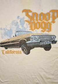 Béžové tričko s grafikou lowrideru se černými a zlatými akcenty. Text zní „Snoop Dogg“ a „California“ ve stylizovaném oranžovém písmu.