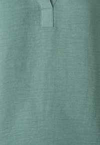 Top turchese chiaro in tessuto testurizzato con scollatura a V e maniche corte, caratterizzato da sottili linee diagonali e una vestibilità rilassata.
