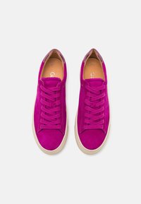 Paire de baskets en daim rose vif avec lacets assortis et semelles en caoutchouc blanches, vue de dessus sur un fond uni.