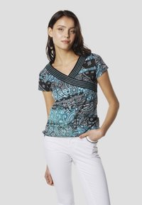 Fekete és türkizkék, paisley mintás, rövid ujjú felső V-nyakkal és texturált csíkokkal. Fehér nadrággal párosítva, deréknál tartva.