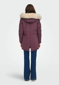 Fioletowa kurtka parka z kapturem obszytym futerkiem, z gorsetem ze sznurkiem w talii i bocznymi rozcięciami, w połączeniu z rozszerzanymi niebieskimi dżinsami.