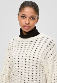 Strickpullover in Creme mit strukturiertem Muster. Unterneath sitzt ein schwarzer Rollkragen, mit lockerer Passform und weitem Ärmeln.