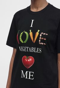 Μαύρο πουκάμισο με κείμενο "I love vegetables", όπου το "love" είναι γραμμένο με τσίλι, αρακά, καρότα και φασόλια, και μια ντομάτα σε σχήμα καρδιάς από κάτω.