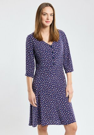 Robe marine avec des manches trois-quarts, dotée d'un décolleté en V, d'une fermeture par boutons et de petits motifs floraux en blanc et rouge. Conception de jupe évasée.