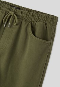Olive green joggery, wykonane z teksturowanej tkaniny, z elastycznym pasem w talii ze sznurkiem i kieszeniami bocznymi.