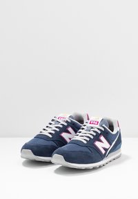 Marinblå sneakers i mesh och mocka, med en vit 'N'-logotyp, grå detaljer och en ljusgrå gummisula. Snörning.