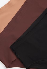 Tri zložené dámske spodné prádlo v béžovej, hnedej a čiernej farbe, usporiadané diagonálne na bielom povrchu.