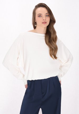 Top bianco a maniche lunghe con una vestibilità ampia e scollatura a barca, abbinato a pantaloni navy a vita alta; texture liscia e colori neutri.