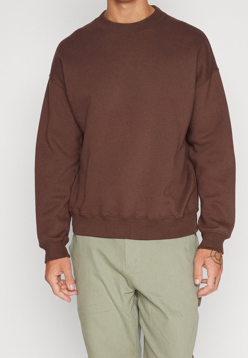 Sudadera de algodón marrón con cuello redondo, hombros caídos y puños de canalé. Presenta un corte relajado y una textura suave.