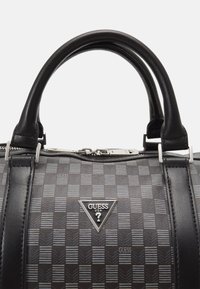 Sac à main noir avec un motif à carreaux, des poignées en cuir, des accessoires en métal argenté et un logo triangulaire proéminent. Couture détaillée et fermeture éclair.