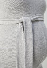Grå ribbet stoff med en myk tekstur har en knytet midje detalj. Plagget fremhever en rund form med et tettsittende design.