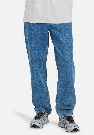 Blue straight-leg denim jeans with a faded finish and visible stitching details. Paired with gray athletic shoes featuring black accents.