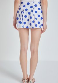 Falda de tela blanca con lunares azules, diseño plisado, largo hasta la mitad del muslo, cintura plana y sandalias doradas minimalistas.