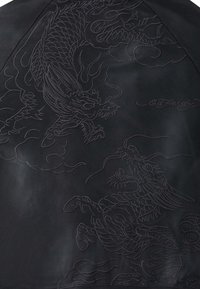 Tela negra con diseños en relieve de dragones y patrones de nubes. Incluye un detallado intrincado y una superficie texturizada. Visible la firma "Ed Hardy".