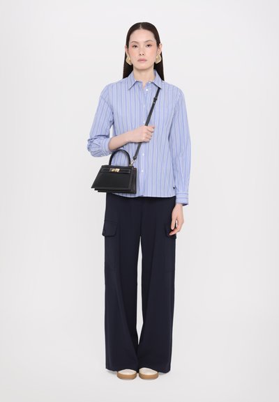 Chemise à rayures bleues à boutons, associée à un pantalon large bleu marine. Accessoirisée avec un petit sac à main noir avec un fermoir en or.