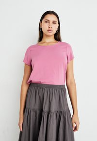 Rosa kortermet t-skjorte med rund hals, sammen med en grå, lagdelt skjørt med elastisk midje, teksturert stoff og flytende design.