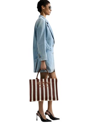 Mujer con blazer de mezclilla azul claro oversized, sosteniendo un bolso tote grande a rayas marrón y blanco con logo "REPLAY", llevando tacones slingback negros.