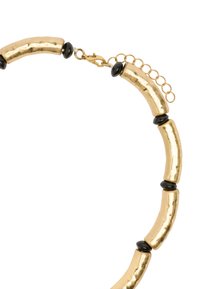 Naszyjnik w kolorze złotym z nierównymi cylindrycznymi ogniwami metalowymi, przeplatany błyszczącymi czarnymi koralikami. Zawiera zapięcie typu homar i łańcuszek wydłużający.