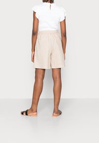 Shorts en lin beige avec une coupe décontractée et une taille élastique. Haut blanc texturé avec des manches courtes à volants. Sandales à glisser noires.