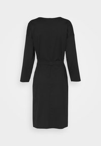 Robe noire longueur genou avec manches longues et ceinture à la taille, vue de dos sur fond blanc uni.