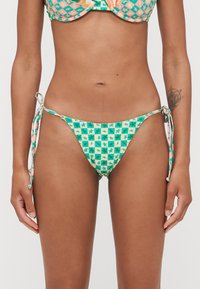 Zöld és sárga bikinialsó csillagmintával, állítható oldalhúzásokkal és struktúrált felülettel. Kifejezetten egy szoros illeszkedéshez tervezve.