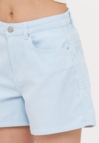 Shorts rayés bleus en tissu à texture lisse ; dotés de poches avant, d'une fermeture à bouton argenté et de détails cousus.