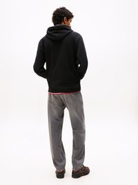 Felpa nera con cappuccio, jeans grigi e scarpe nere con accenti rossi. Materiale morbido con vestibilità rilassata, cuciture visibili sui jeans.
