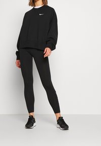 Black Nike oversized sweatshirt with white logo, combined with black fitted leggings and black athletic shoes, all set against a neutral background.
