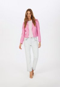 Pink cropped blazer with two buttons, paired with a light pink top and light blue distressed jeans. Woman wears gold heeled sandals.