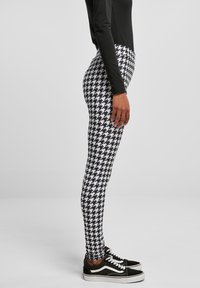 Leggings en pied-de-poule noir et blanc en tissu extensible, associés à des baskets noires avec des accents et des lacets blancs.