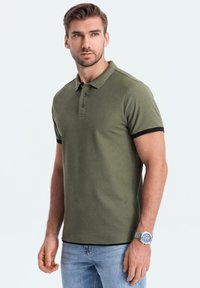 Oliveově zelená polo tričko s černým límečkem a akcenty na rukávech. Slim fit design, krátké rukávy a tříknoflíková léga. Texturovaná látka.