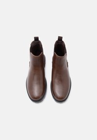 Bocanci din piele maro, la nivelul gleznei, cu un finisaj neted, panouri laterale elastice și mânere pentru a-i trasa, având o talpă din cauciuc rezistentă.