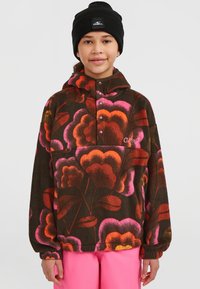 Pull en polaire à motif floral en rose, orange et brun, avec une patte de boutonnage à mi-hauteur et des poignets élastiqués. Porté avec un bonnet noir.