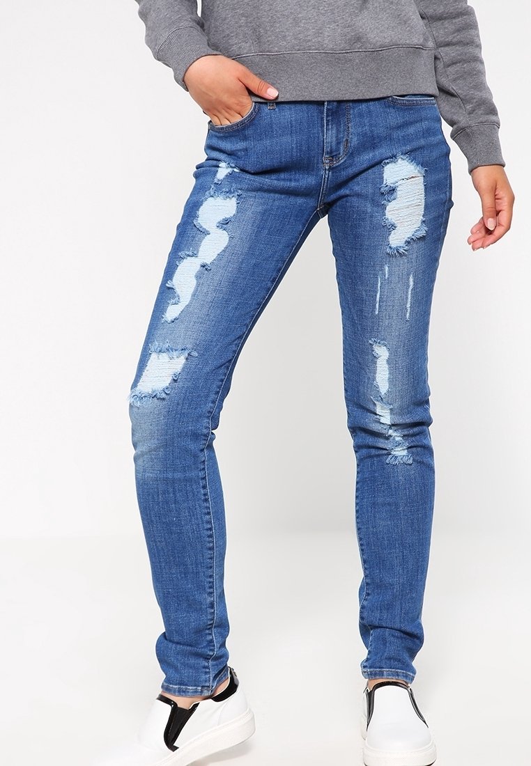 Jean skinny bleu avec des endroits usés et des bords effilochés. Confectionné en tissu denim, avec cinq poches et une taille mi-haute.