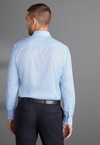 Helles blaues Langarmhemd mit einem Button-Down-Kragen, aus Baumwollstoff, und dunkelblauen Hosen, die zwei Gesäßtaschen mit Knopfakzenten aufweisen.