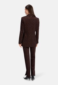 Brown and black patterned suit with a chevron design; features a notch lapel, single button detail, and tailored fit. Slim pant legs with slits.