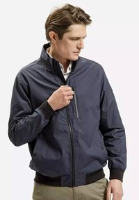 Bomberka w kolorze granatowym, wykonana z gładkiego materiału, z wysokim kołnierzem, zapinaną na zamek kieszenią na piersi oraz kieszeniami bocznymi, z ściągaczami przy mankietach i u dołu.