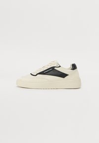 Basket en cuir crème avec un panneau noir texturé, bout rond, semelle plate et couture ton sur ton ; dispose d'une fermeture à lacets et de détails de marque.
