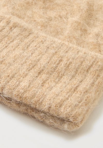 Primer plano de tela de punto beige suave y peluda con textura acanalada a lo largo del borde, probablemente parte de un suéter o prenda similar.