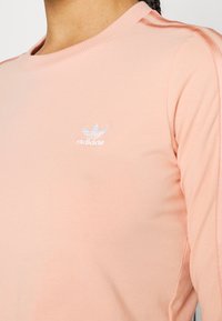 Light pink long-sleeve shirt made of soft fabric, featuring a round neckline and a small white Adidas logo embroidered on the chest.