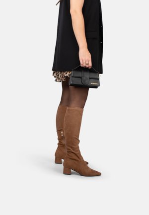 Braune Wildleder-Stiefel bis zum Knie mit spitzer Zehenpartie und Blockabsatz, die mit einem Reißverschluss an der Seite versehen sind, kombiniert mit einer schwarzen Tasche.