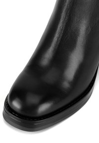 Čierne kožené členkové topánky s okrúhlou špicou, lesklou textúrou, minimálnym prešívaním a hrubou plochou podrážkou.