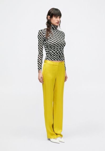 Čierno-biely vzorovaný rolák v kombinácii so žltými širokými nohavicami a bielymi topánkami so špicatou špičkou.