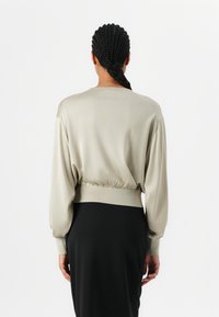 Hellbeige, tief ausgeschnittener Pullover aus einem weichen Material mit langen Ärmeln und gerafftem Saum. Kombiniert mit einem eleganten schwarzen Rock.