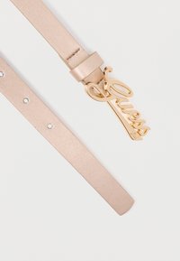 Ζώνη από απαλό ροζ συνθετικό δέρμα με γυαλιστερή χρυσή αγκράφα με λογότυπο "Guess" σε καλλιγραφικό στυλ και μεταλλικά καρφιά κατά μήκος του ιμάντα.